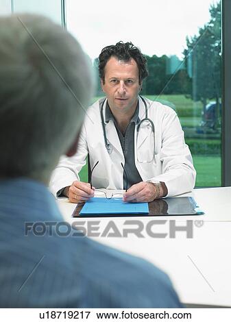 Stock Photo - Male doctor at his desk talking with mature male patient.. Fotosearch