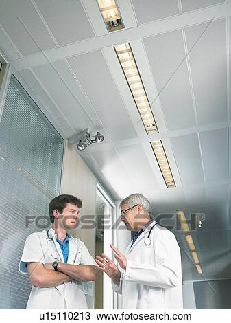 Stock Image - Mature doctor and young doctor in discussion in a lobby of a hospital low angle.. Fotosearch