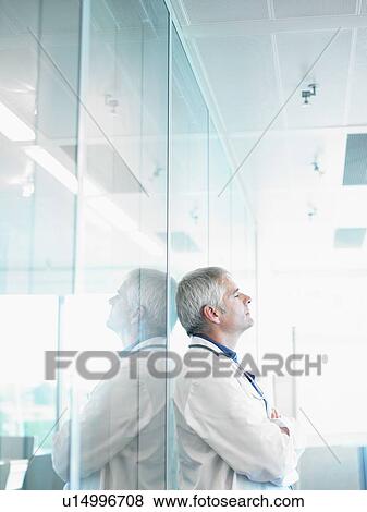 Relaxed doctor leaning on glass wall in hospital lobby. View Large Photo Image Stock Photo - Relaxed doctor leaning on glass wall in hospital lobby.. Fotosearch