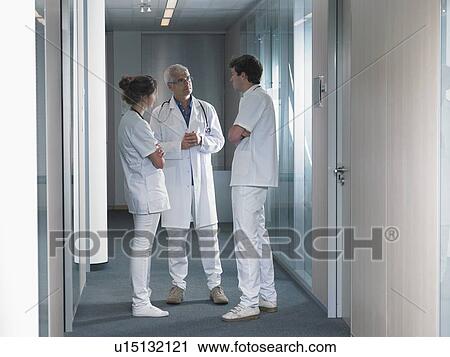 Stock Image - Three doctors in discussion in hospital lobby... Fotosearch