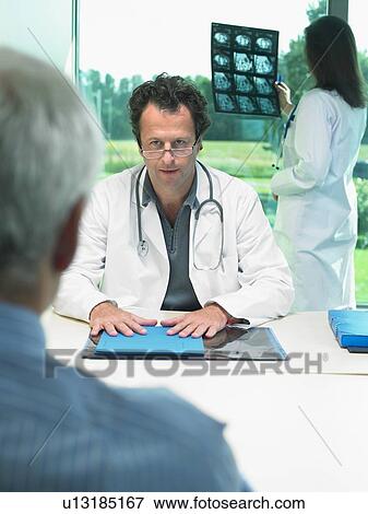 Two doctors discussing x-rays with mature patient. View Large Photo Image Stock Photo - Two doctors discussing x-rays with mature patient.. Fotosearch