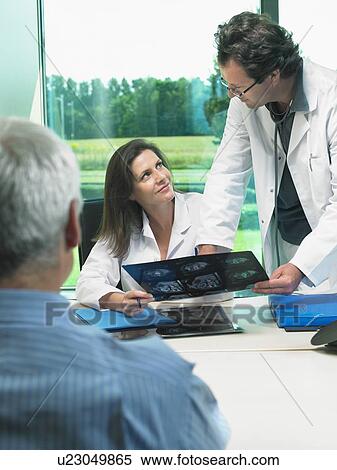Two doctors discussing x-rays with mature patient. View Large Photo Image Stock Photography - Two doctors discussing x-rays with mature patient.. Fotosearch