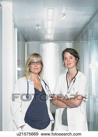 Two female doctors looking at camera in a lobby of a hospital smiling. Portrait. View Large Photo Image Stock Photo - Two female doctors looking at camera in a lobby of a hospital smiling. Portrait.. Fotosearch