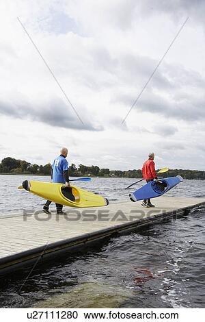 Stock Image - Two senior men carrying kayaks. Fotosearch