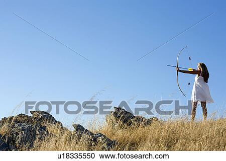 Stock Image - Young woman arrow shooting in field. Fotosearch