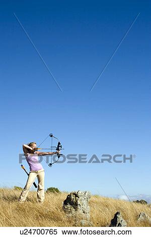 Stock Photography - Young woman arrow shooting in field. Fotosearch