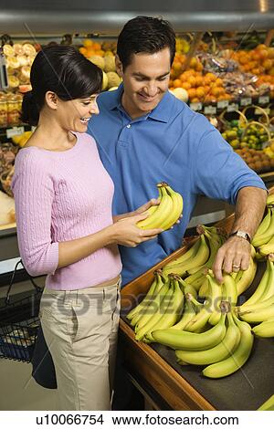 Picture - Caucasian mid-adult couple grocery shopping for bananas.. Fotosearch