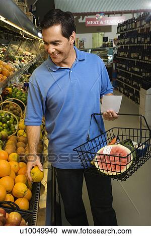 Stock Image - Caucasian mid-adult male grocery shopping for fruit.. Fotosearch