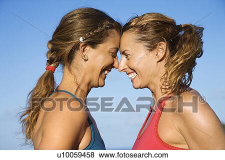 Stock Photo - Caucasian mid-adult women with heads together smiling.. Fotosearch