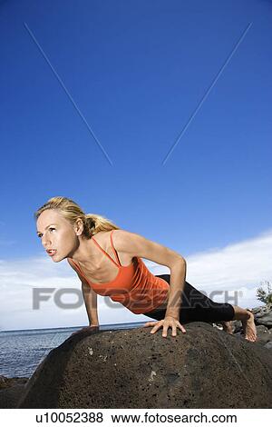 Stock Photo - Caucasian young adult woman doing push up on rock.. Fotosearch