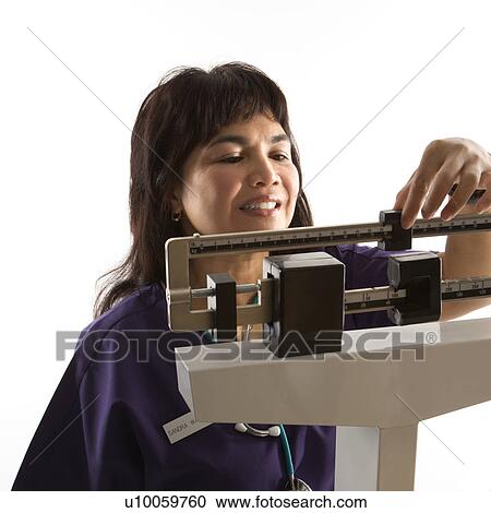 Stock Image - Middle-aged female Filipino nurse reading weight on scale.. Fotosearch
