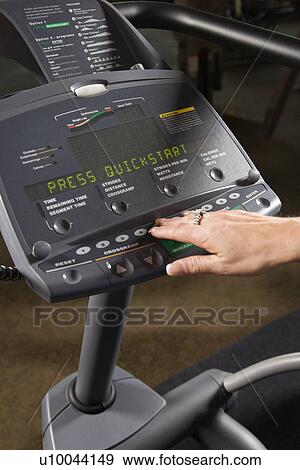Stock Photo - Prime adult Caucasian female setting up elliptical machine at gym.. Fotosearch