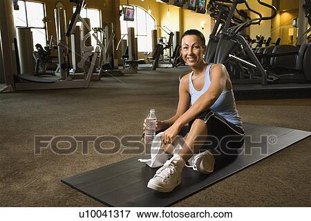 Prime adult Caucasian female sitting on mat on gym floor. View Large Photo Image Stock Photo - Prime adult Caucasian female sitting on mat on gym floor.. Fotosearch
