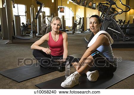 Stock Image - Prime adult Caucasian female with personal trainer at gym.. Fotosearch