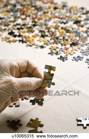 Stock Photography - Close-up of Elderly Caucasian woman's hand holding puzzle piece.. Fotosearch