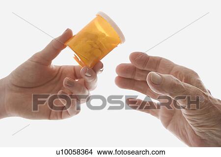 Picture - Close-up of mid-adult Caucasian female's hand handing medication bottle to elderly Caucasian male hand.. Fotosearch