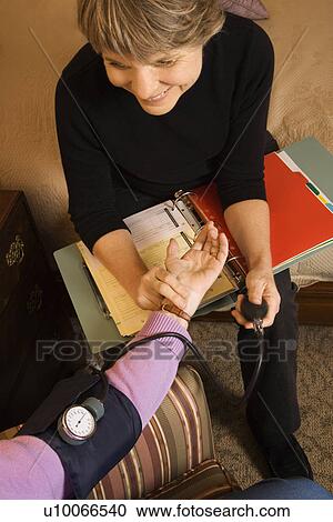 Stock Image - Elderly Caucasian woman at retirement community center receiving blood pressure test by nurse.. Fotosearch