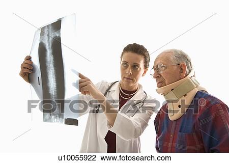 Stock Image - Mid-adult Caucasian female doctor ponting at x-ray with elderly Caucasian male in neck brace looks on.. Fotosearch