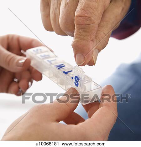 Stock Image - Mid-adult Caucasian female hands holding medication case for an elderly Caucasian male.. Fotosearch