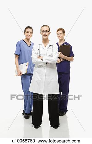 Stock Image - Full-length portrait of Caucasian women healthcare workers in uniforms standing against white background.. Fotosearch