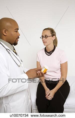 Mid-adult African-American doctor explaining medication to Caucasion mid-adult female patient. View Large Photo Image Picture - Mid-adult African-American doctor explaining medication to Caucasion mid-adult female patient.. Fotosearch