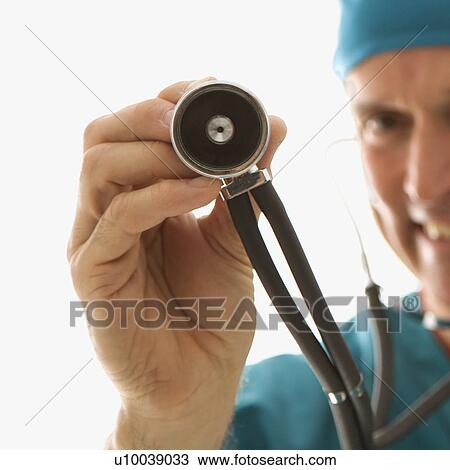 Stock Image - Mid-adult Caucasian male doctor in scrubs holding a stethoscope out towards viewer.. Fotosearch