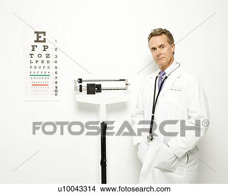 Mid-adult Caucasian male doctor standing next to scale with eye chart on wall. View Large Photo Image Picture - Mid-adult Caucasian male doctor standing next to scale with eye chart on wall.. Fotosearch