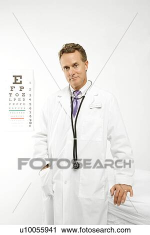 Stock Image - Mid-adult Caucasian male doctor with eye chart in background.. Fotosearch