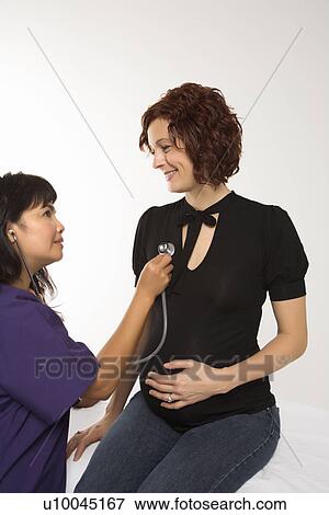 Stock Photo - Pregnant Caucasian mid-adult woman having vital signs checked by nurse.. Fotosearch