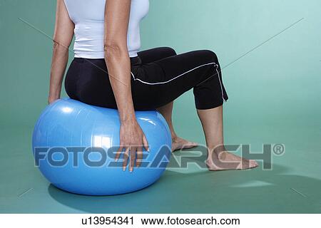 Stock Image - Mature woman sitting on Swiss ball (close-up). Fotosearch