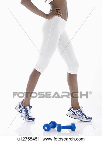 Stock Image - Young woman with dumbbells stretching (low section). Fotosearch