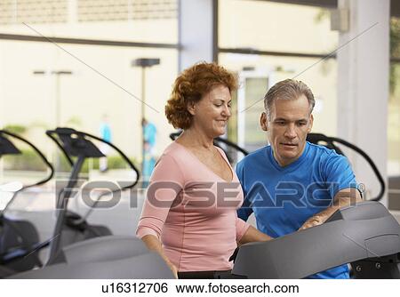 Stock Photograph - Man helping woman with treadmill. Fotosearch