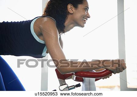 Stock Image - Young woman indoor cycling. Fotosearch
