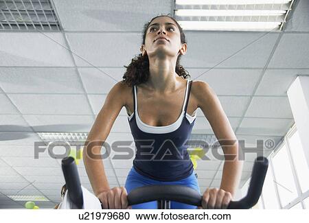 Stock Image - Young woman indoor cycling. Fotosearch