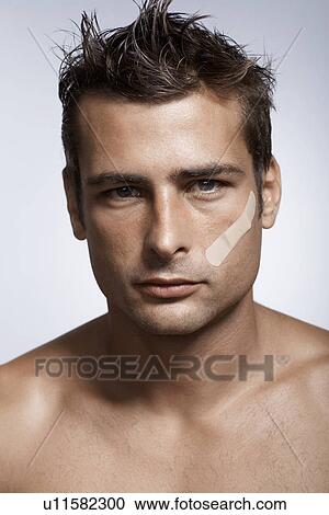 Stock Image - Mid adult man with adhesive plaster on cheek. Fotosearch