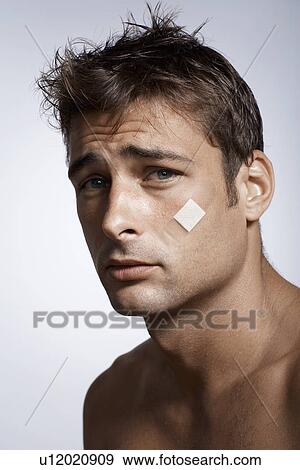 Stock Photo - Mid adult man with adhesive plaster on cheek. Fotosearch