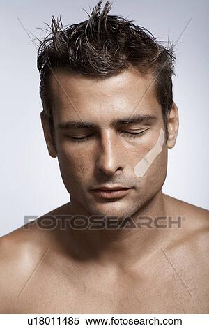 Stock Photography - Mid adult man with adhesive plaster on cheek. Fotosearch