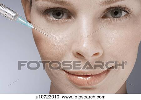 Stock Image - Syringe near woman's face, close-up. Fotosearch