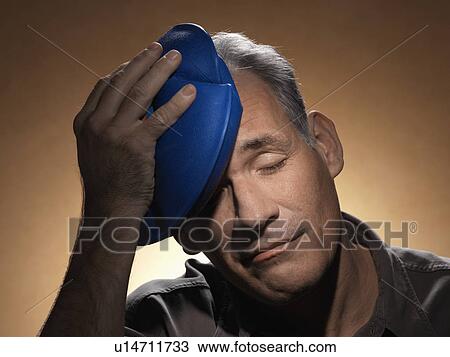 Stock Image - Man holding ice pack on head. Fotosearch