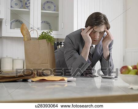 Businessman with bag of groceries rubbing forehead in kitchen View Large Photo Image Picture - Businessman with bag of groceries rubbing forehead in kitchen. Fotosearch