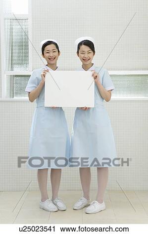 Stock Image - Portrait of two nurses, twin sisters, holding a blank board, front view. Fotosearch