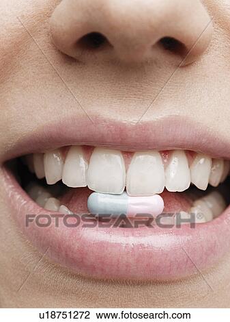 Stock Image - Woman holding vitamin pill in teeth. Fotosearch