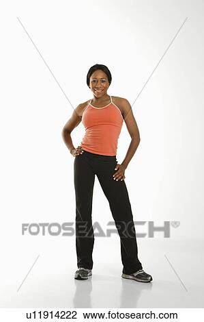Stock Image - African American young adult woman in athletic wear smiling at viewer with hands on hips.. Fotosearch