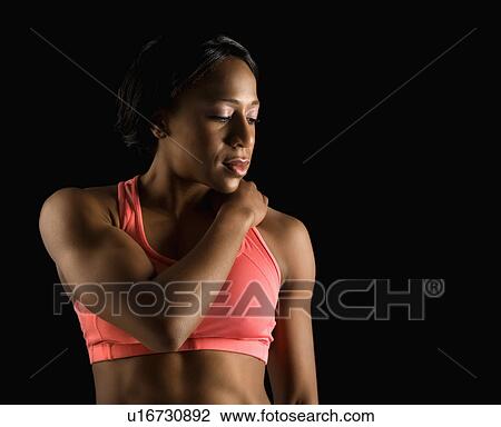 Stock Image - African American young adult woman in sports bra with hand on shoulder and eyes closed.. Fotosearch