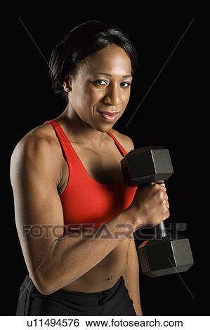 Stock Photograph - African American young adult woman holding dumbbell and looking at viewer.. Fotosearch