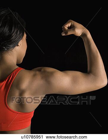Stock Image - Back view of African American woman flexing muscular bicep.. Fotosearch