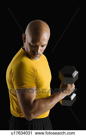 Mid adult multiethnic man wearing yellow exercise shirt doing arm curls while looking at bicep. View Large Photo Image Stock Image - Mid adult multiethnic man wearing yellow exercise shirt doing arm curls while looking at bicep.. Fotosearch
