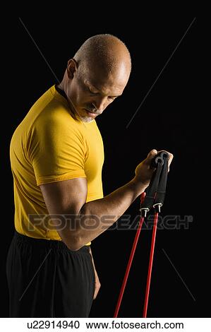 Mid adult multiethnic man wearing yellow exercise shirt exercising with stretch band and looking at bicep. View Large Photo Image Stock Image - Mid adult multiethnic man wearing yellow exercise shirt exercising with stretch band and looking at bicep.. Fotosearch