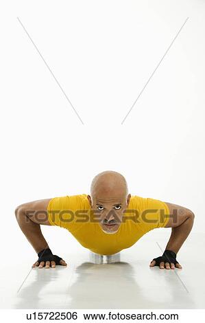 Stock Photograph - Mid adult multiethnic man wearing yellow exercise shirt doing pushups while looking at viewer.. Fotosearch