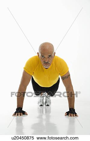 Stock Photography - Mid adult multiethnic man wearing yellow exercise shirt doing pushups while looking at viewer.. Fotosearch